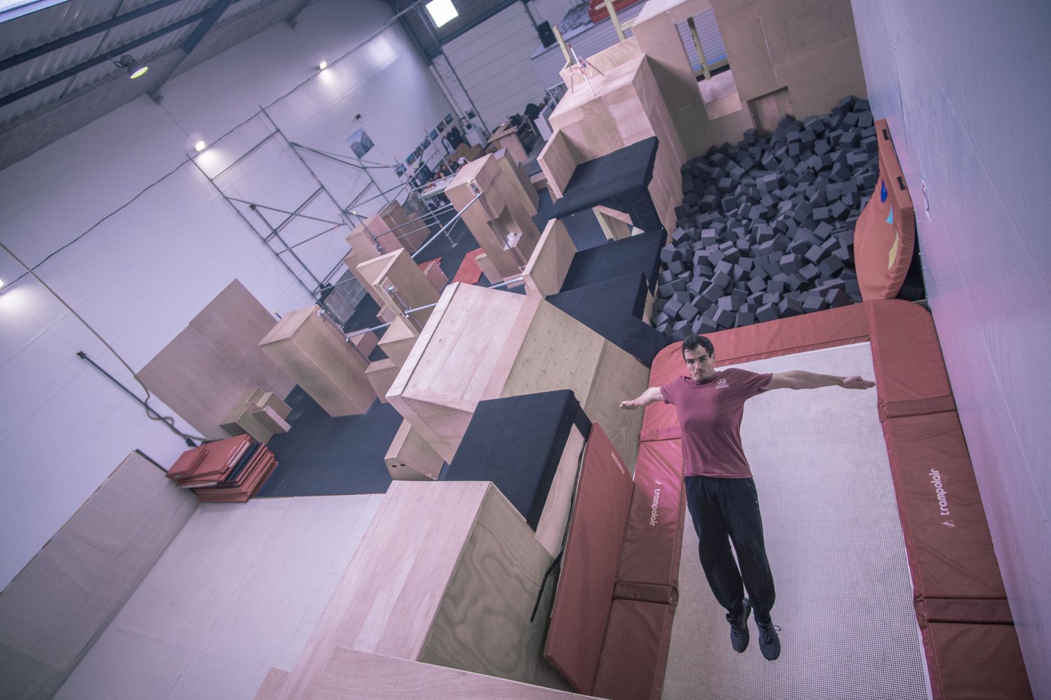 Athlète en vol, bras écartés, au-dessus des trampolines de la salle